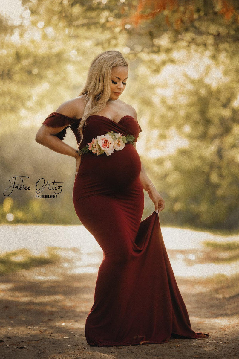 Expecting mother wearing the Arianna gown in burgundy by Sew Trendy standing on garden path.