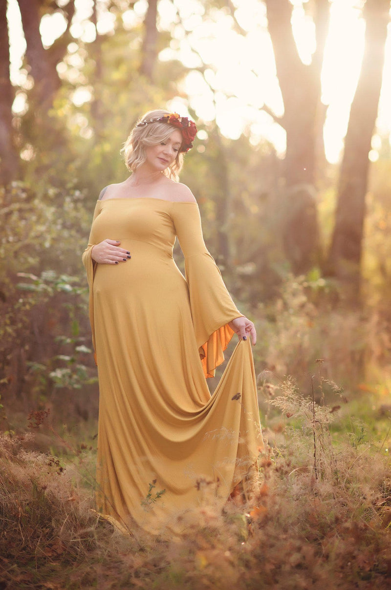 Expecting mother wearing the Gwen gown in gold by Sew Trendy standing in a field at golden hour
