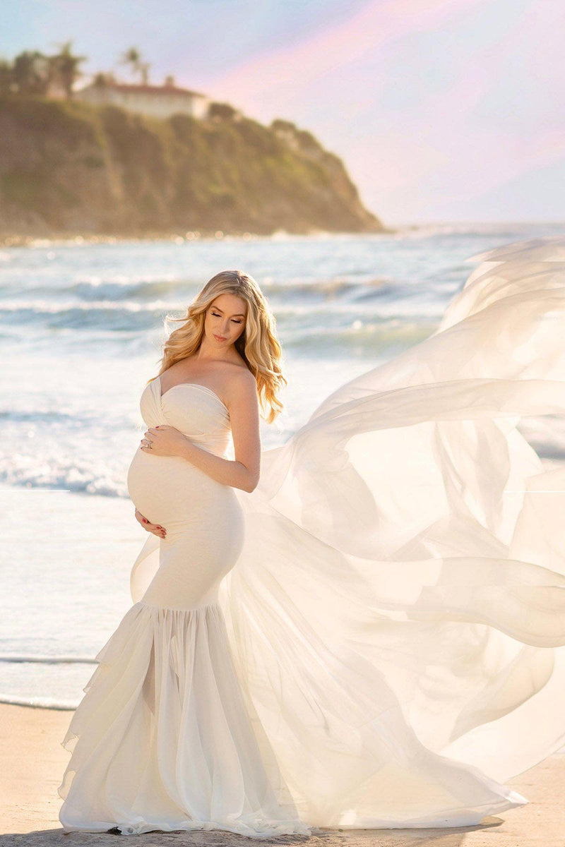 Pregnant mother in the Liv Gown by Sew Trendy Accessories in Ivory standing on the beach.