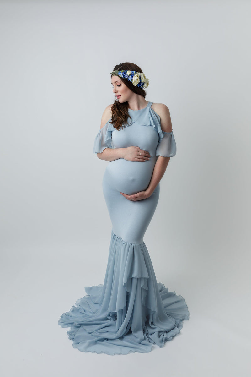 Pregnant woman in the Sariah Gown in Blue Rain by Sew Trendy Accessories standing in the studio on a light gray backdrop.