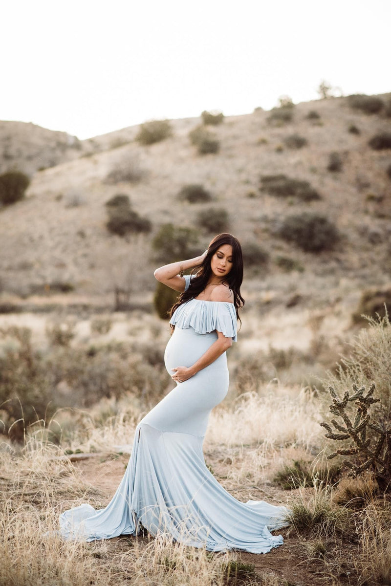Pregnant Latina woman wearing the Cirenya gown in blue rain by Sew Trendy, standing in a desert field.