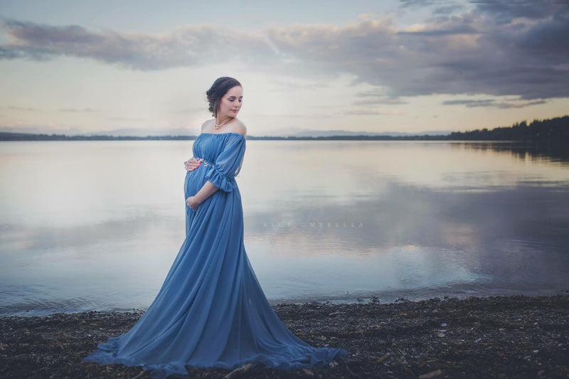 Pregnant Woman in the Paulina Gown in Blue Steel by Sew Trendy Accessories standing at a lake with water in the background.