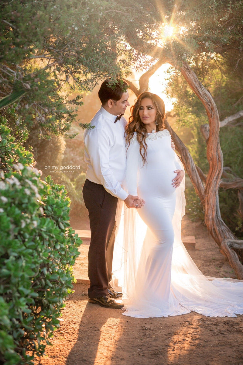 Beautiful pregnant woman wearing the Ravenna bridal mesh cape over her Sew Trendy gown in White standing with her husband at sunset