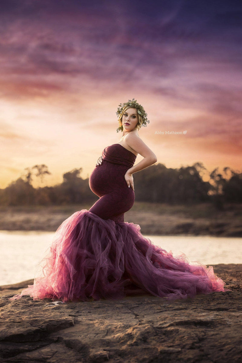 Pregnant woman wearing Celine gown in plum by Sew Trendy standing near lake at sunset