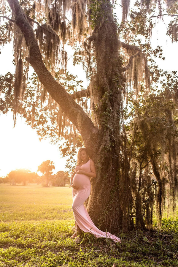 Expecting mother wearing the Courtney gown in dusty pink standing under a willow tree at sunset