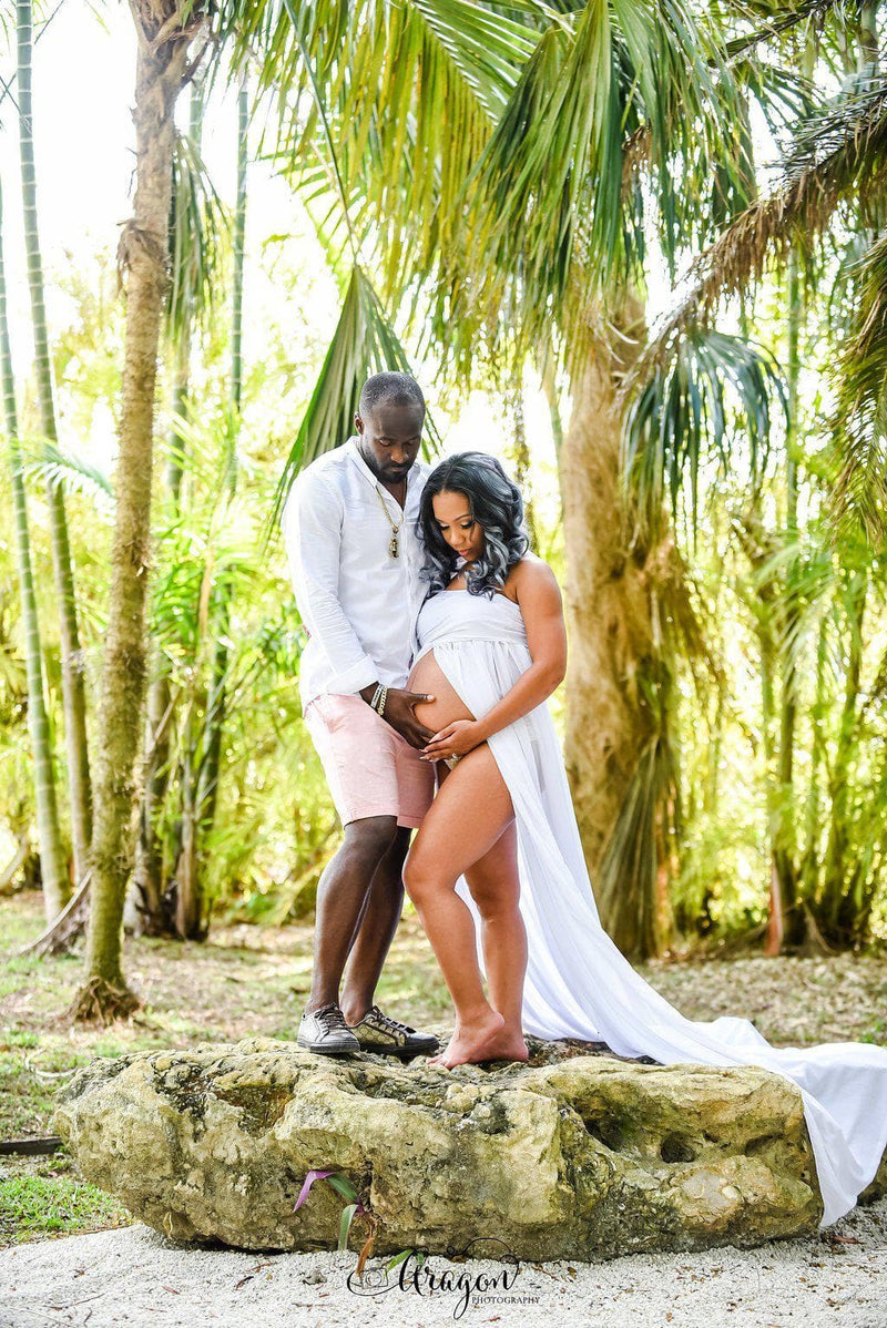 Pregnant Woman in the Rachel Gown in Ivory by Sew Trendy Accessories standing with a man in front of palm trees.