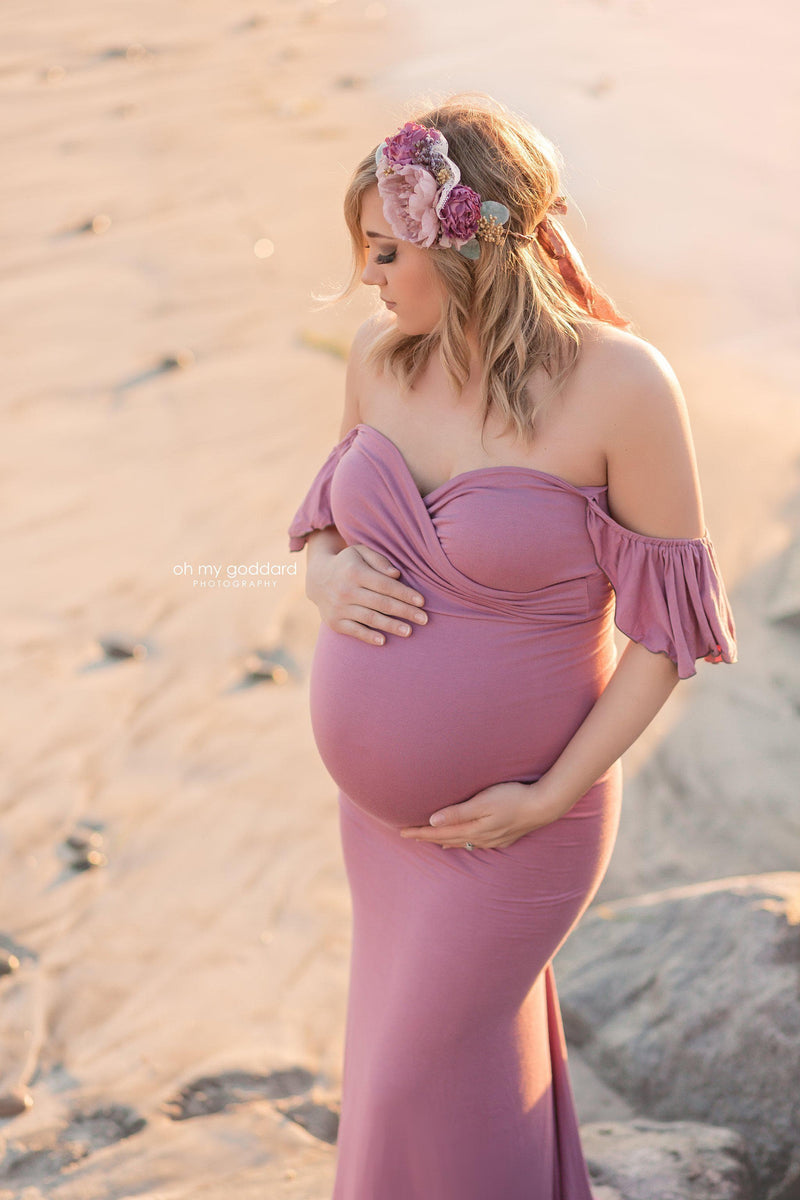 Expecting mother wearing the Arianna gown in Orchid by Sew Trendy standing on the beach.