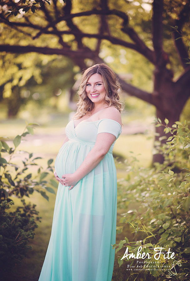 Pregnant mother in the Lexcie Gown by Sew Trendy Accessories in pale mint standing in front of trees.