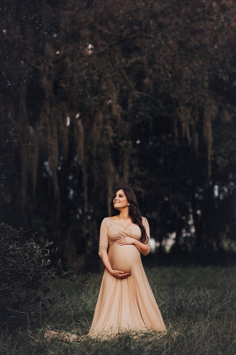 Expecting mother wearing Brady gown in camel by Sew Trendy, standing in tree grove.