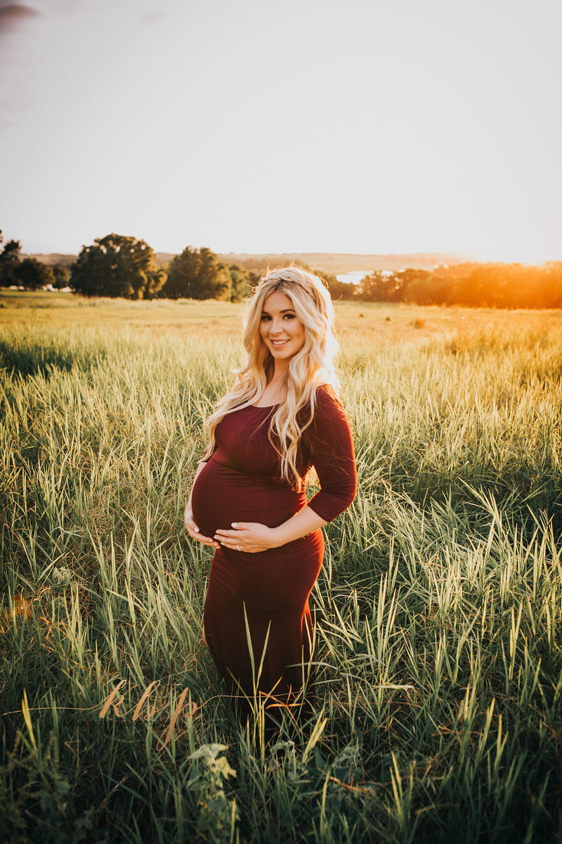 Pregnant woman wearing the Ember gown in brick by Sew Trendy standing in field at sunset