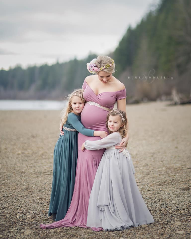 Beautiful expecting mother wearing the Allysa by Sew Trendy embracing her daughters, standing next to lake in winter.