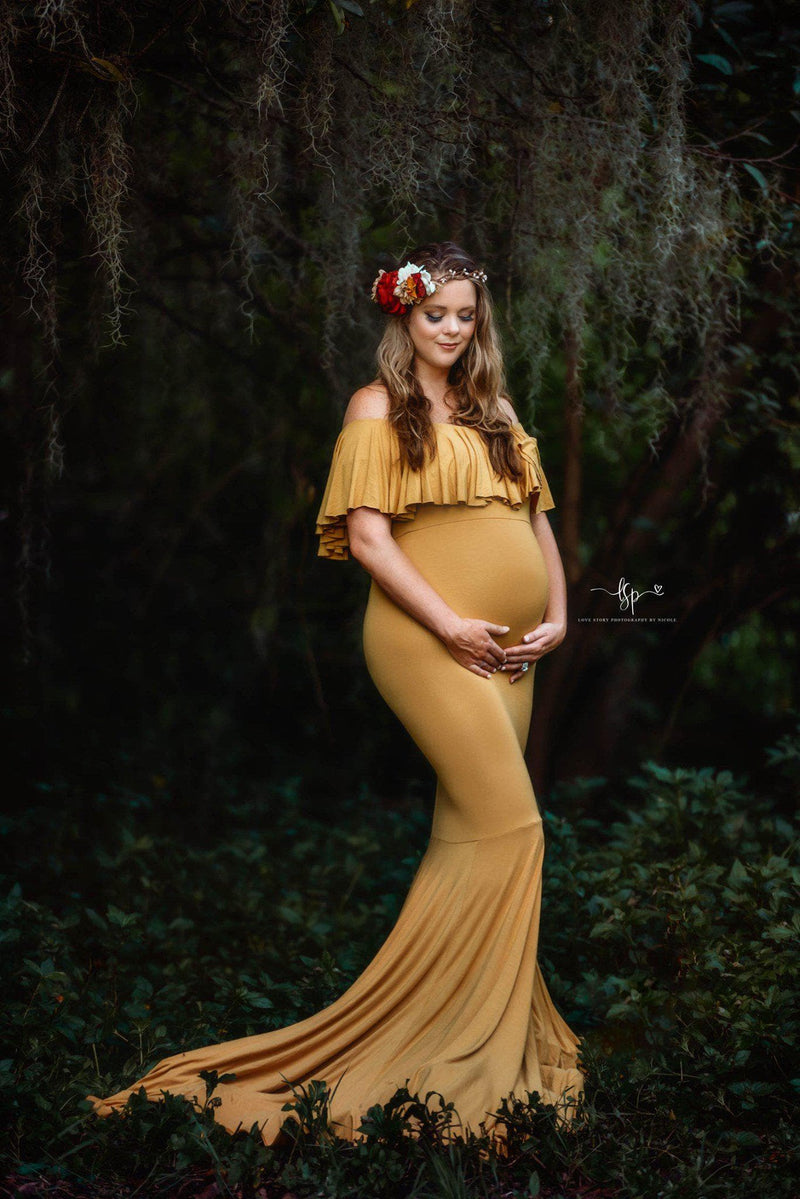 Pregnant woman wearing the Cirenya gown in gold by Sew Trendy, standing under willow tree with flowers in hair.