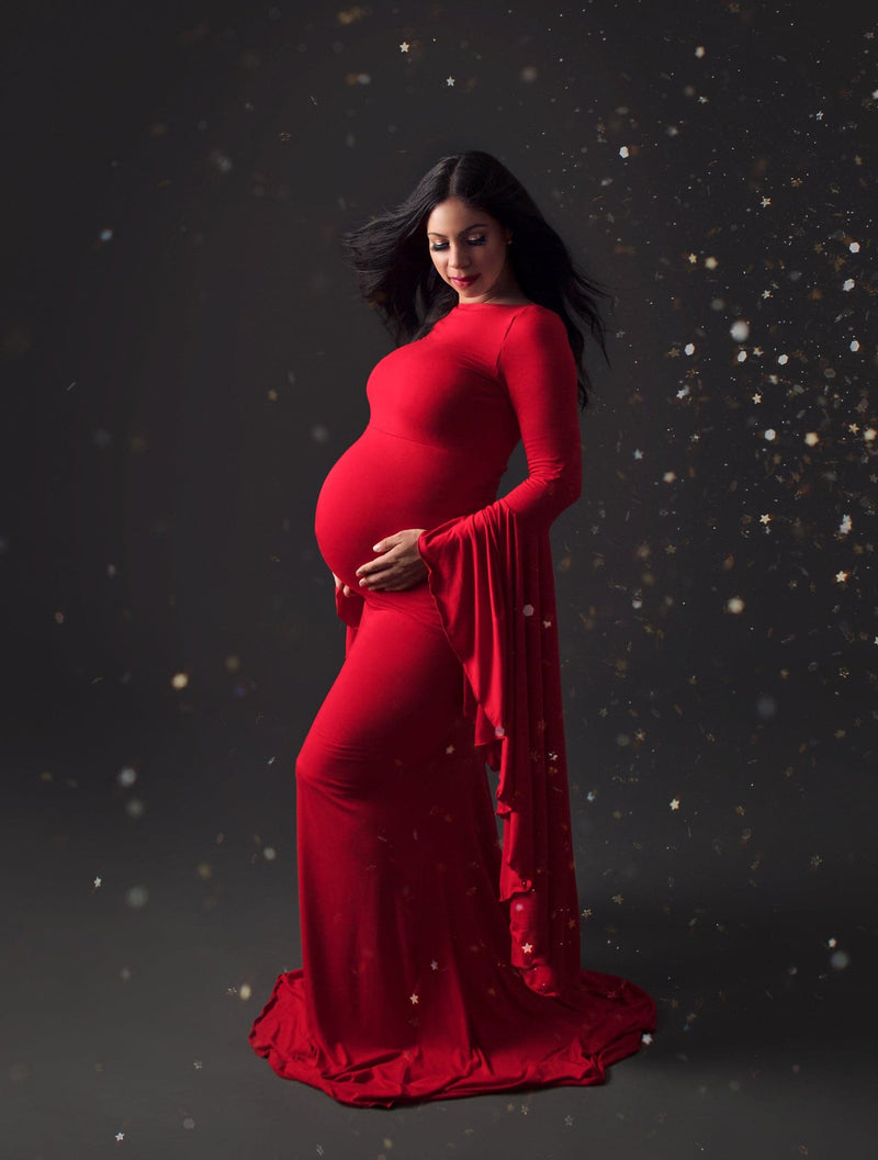 Beautiful expecting mother in red Sew Trendy Marisol gown standing in studio with twinkle lights