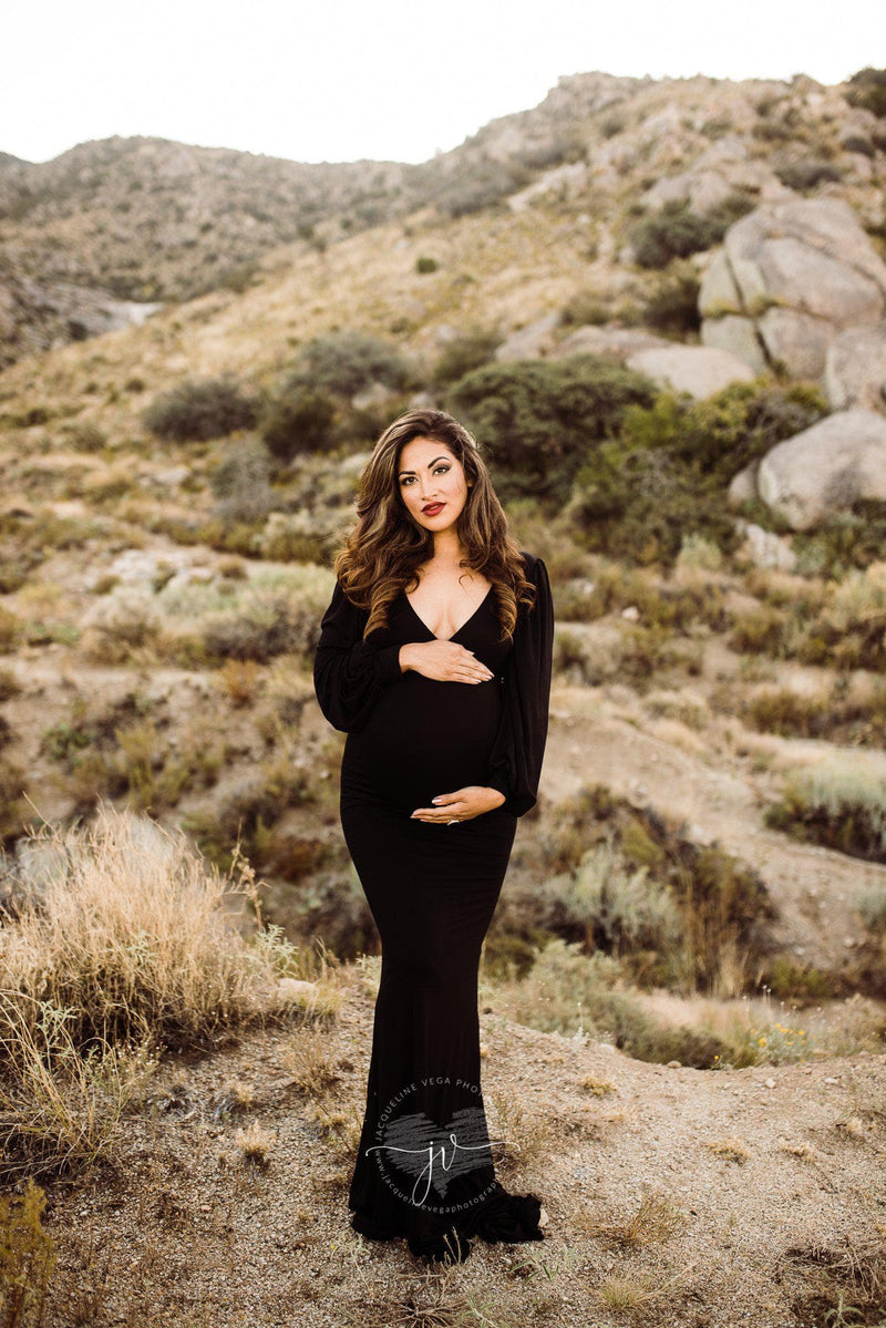 Pregnant woman wearing the Florence gown in black by Sew Trendy standing in desert at sunset