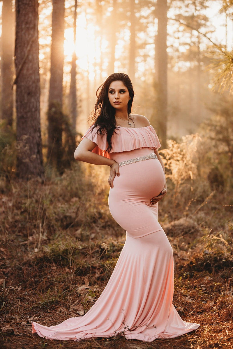 Pregnant brunette woman wearing the Cirenya gown in blush by Sew Trendy, standing in a sunlit forest 