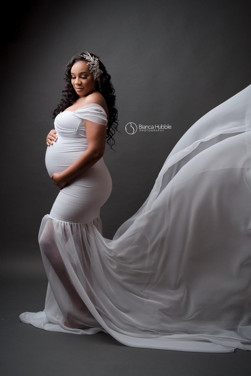 Expecting mother wearing the Angela gown in white by Sew Trendy standing on grey backdrop in studio.