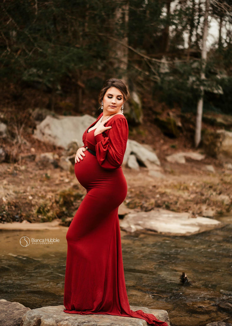 Pregnant woman wearing the Florence gown in brick by Sew Trendy standing near river at sunset
