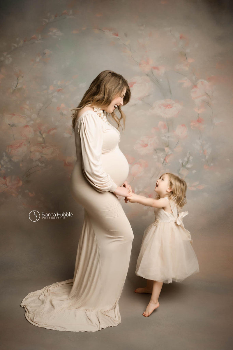 Pregnant woman wearing the Florence gown in champagne by Sew Trendy standing in studio with daughter on floral backdrop