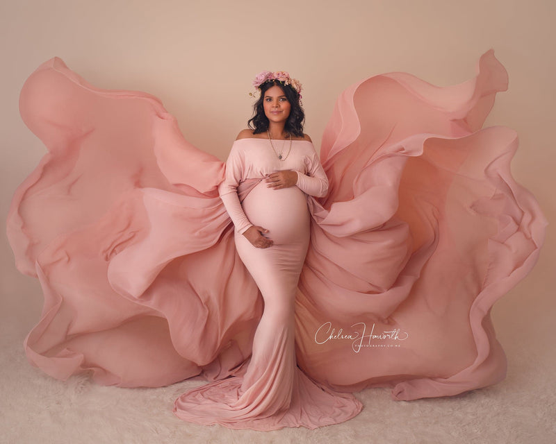 Expecting mother wearing the Jaden gown and detachable waterfall tossing train by Sew Trendy in a neutral colored photography studio