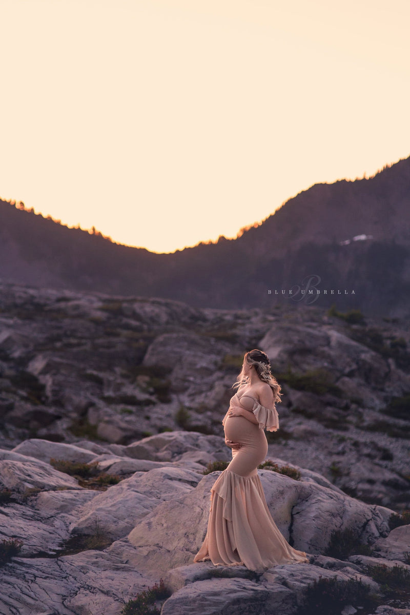 Pregnant woman in the Sable Gown in Camel by Sew Trendy Accessories standing with mountains in the background.