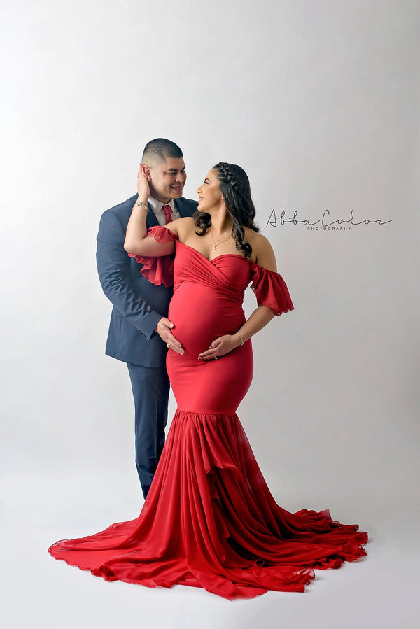 Expecting mother wearing the Sable gown in red by Sew Trendy standing with her husband iin studio