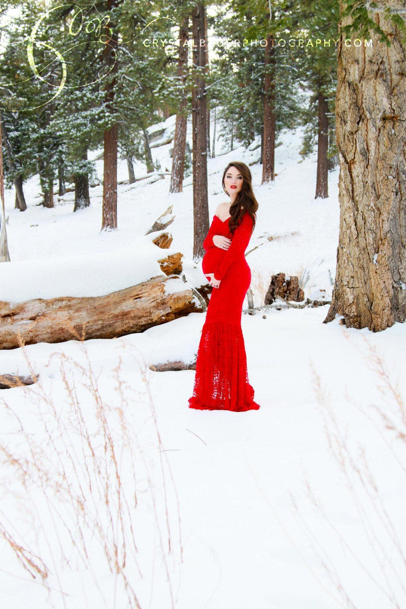 Pregnant woman in the Priscilla Gown in Red by Sew Trendy Accessories standing in the snow with trees in the background.