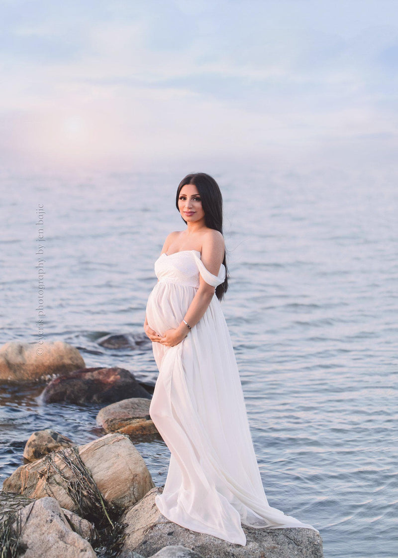 Pregnant mother wearing the Alina gown by Sew Trendy in ivory standing the ocean at sunrise