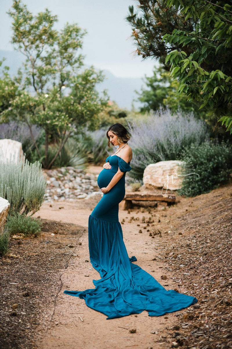 Expecting mother wearing the Angela gown in teal by Sew Trendy, standing on garden path.