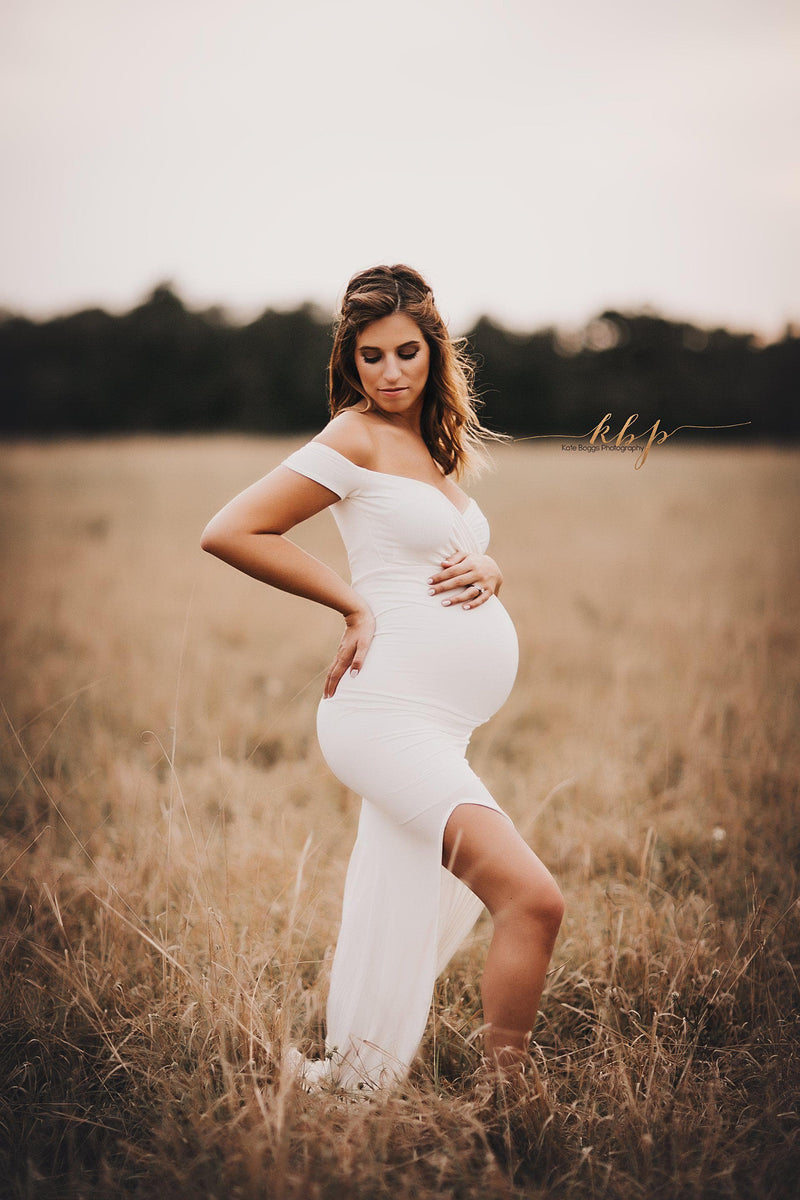 Pregnant woman wearing the audrey gown in ivory by Sew Trendy with side split, standing in sunlit field.
