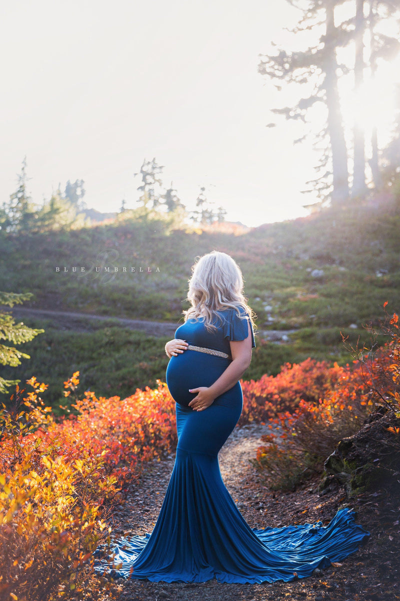 Pregnant woman wearing the bonnie gown in teal by Sew Trendy, standing in autumn field.