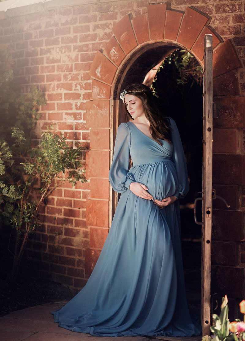Pregnant mother wearing Brigitte gown in steel blue by Sew Trendy standing in garden archway
