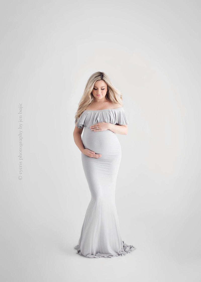 Expecting mother wearing the Colbie gown in grey by Sew Trendy standing in backlit studio