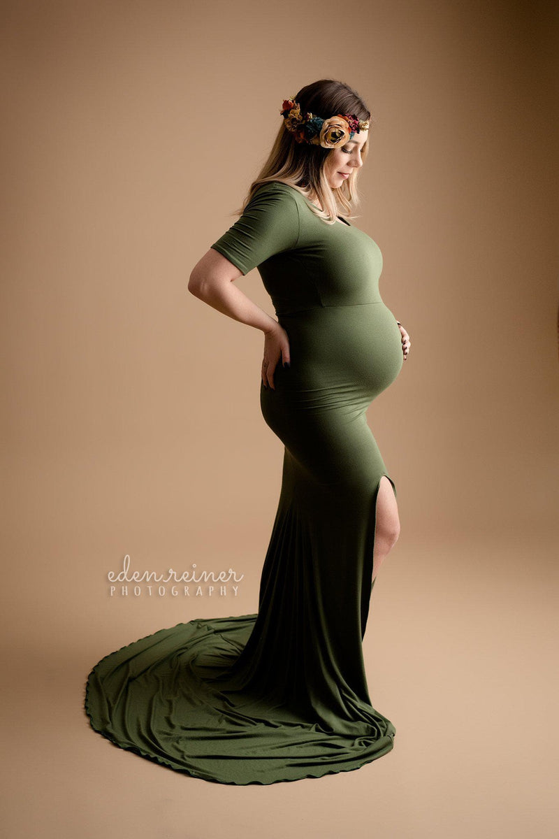 Pregnant woman wearing the Ember gown in evergreen by Sew Trendy standing in studio on pecan backdrop