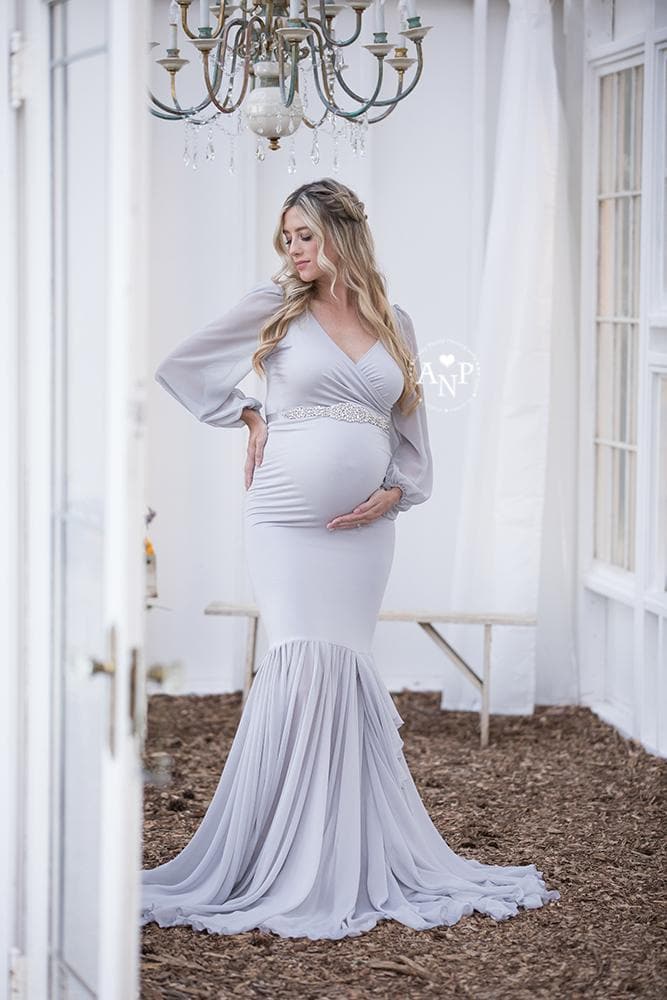 Pregnant mother wearing the Francis gown in grey by Sew Trendy standing under chandelier in studio
