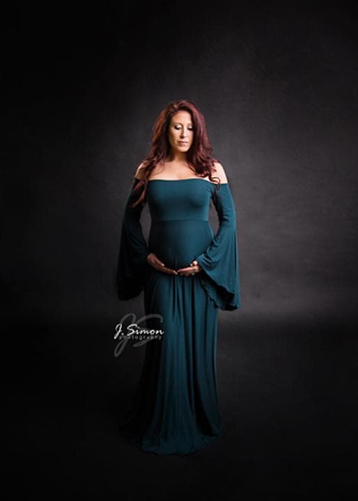 Expecting mother wearing the Gwen gown in blue spruce by Sew Trendy standing in studio on charcoal backdrop