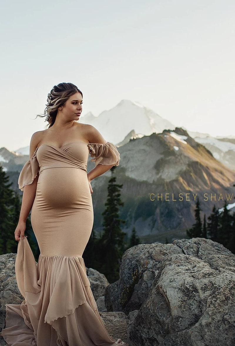 Pregnant woman in the Sable Gown in Camel by Sew Trendy Accessories standing with mountains in the background.