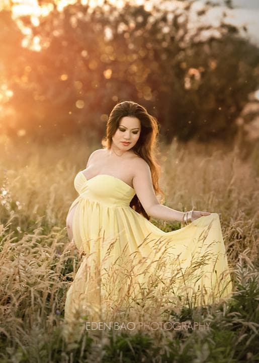 Pregnant woman in the Raquel Gown in Yellow by Sew Trendy Accessories standing in a field with tall grass.