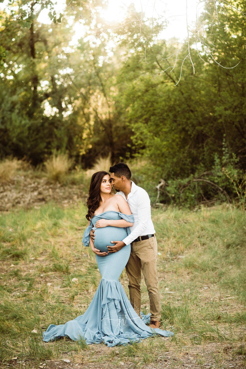Pregnant woman in the Sable Gown in Sage by Sew Trendy Accessories standing with a man with trees in the background.