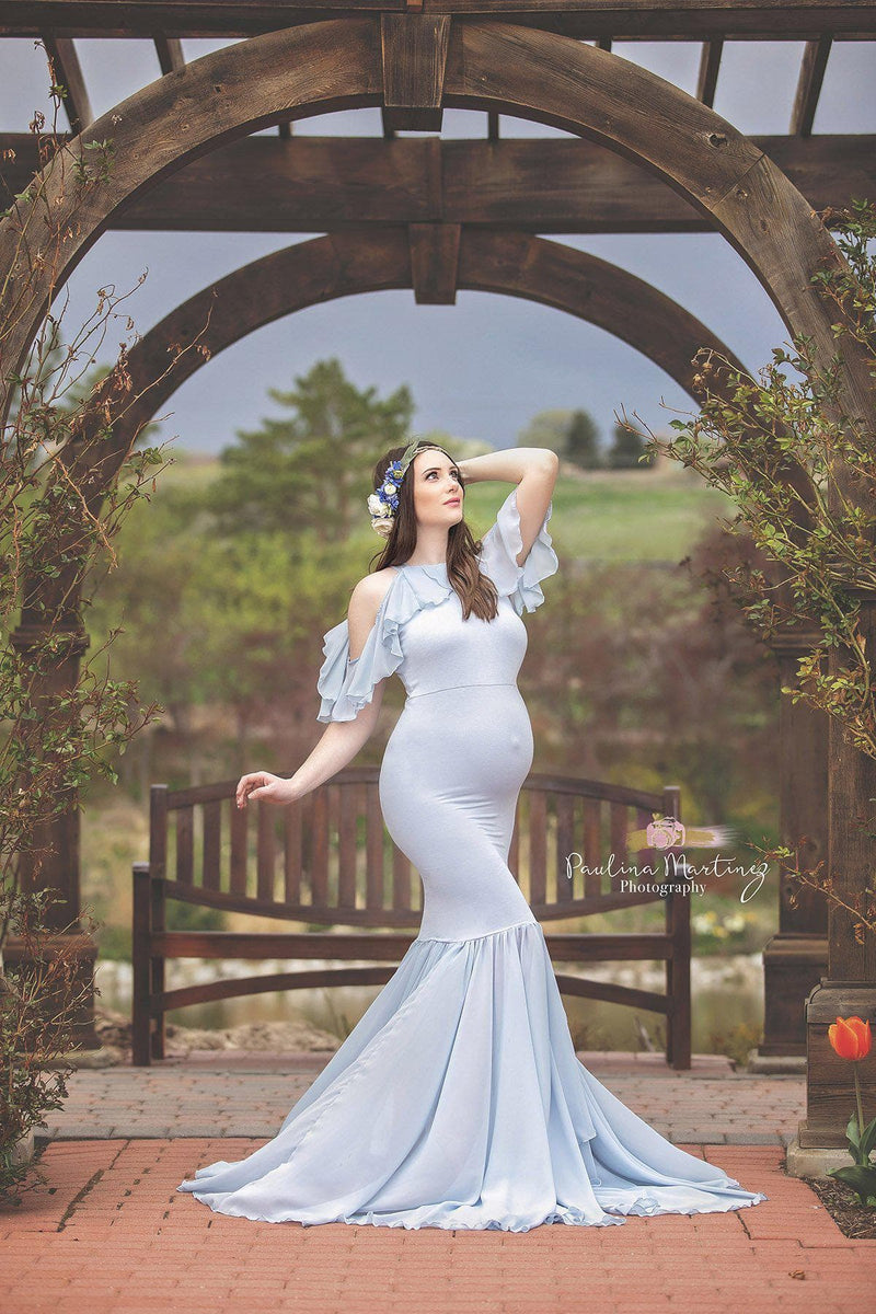 Pregnant woman in the Sariah Gown in Blue Rain by Sew Trendy Accessories standing in front of a wooden archway in a garden.