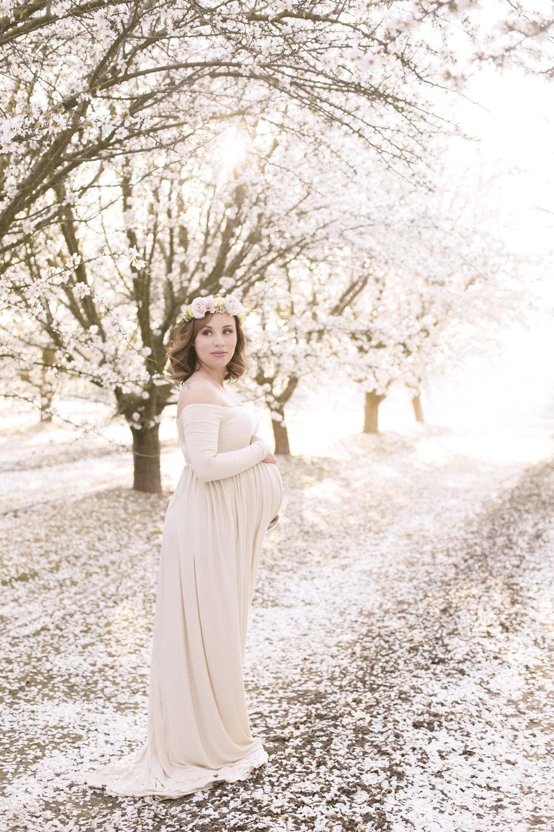 Pregnant woman in the Miriam Gown in Blush by Sew Trendy Accessories standing on a path with tree blossoms.