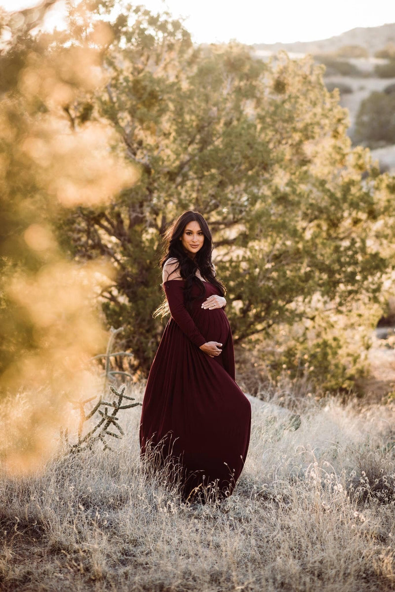 Pregnant woman in the Miriam Gown in Burgundy by Sew Trendy Accessories standing in a golden field.