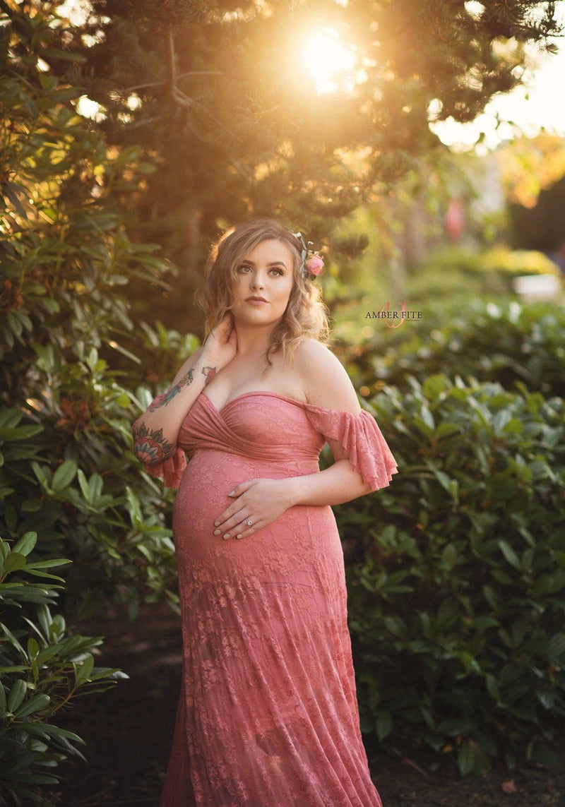 Pregnant woman in the Persephone Gown in Antique Rose by Sew Trendy Accessories standing in front of green bushes.