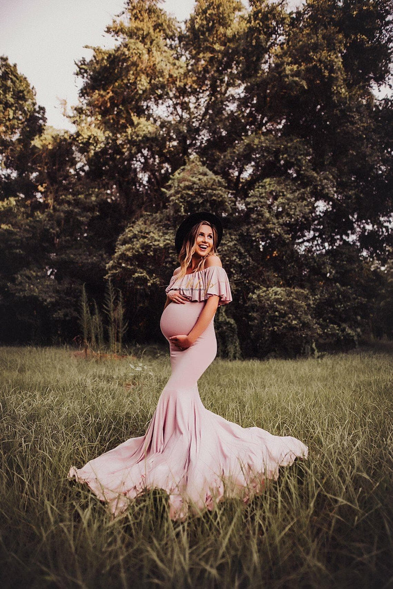 Pregnant woman wearing the Cirenya gown in mauve by Sew Trendy, standing in field with a black hat.