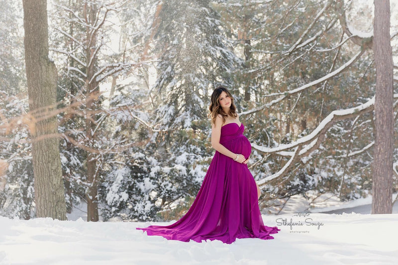 Pregnant woman in the Raquel Gown in Magenta by Sew Trendy Accessories standing in the snow with trees.