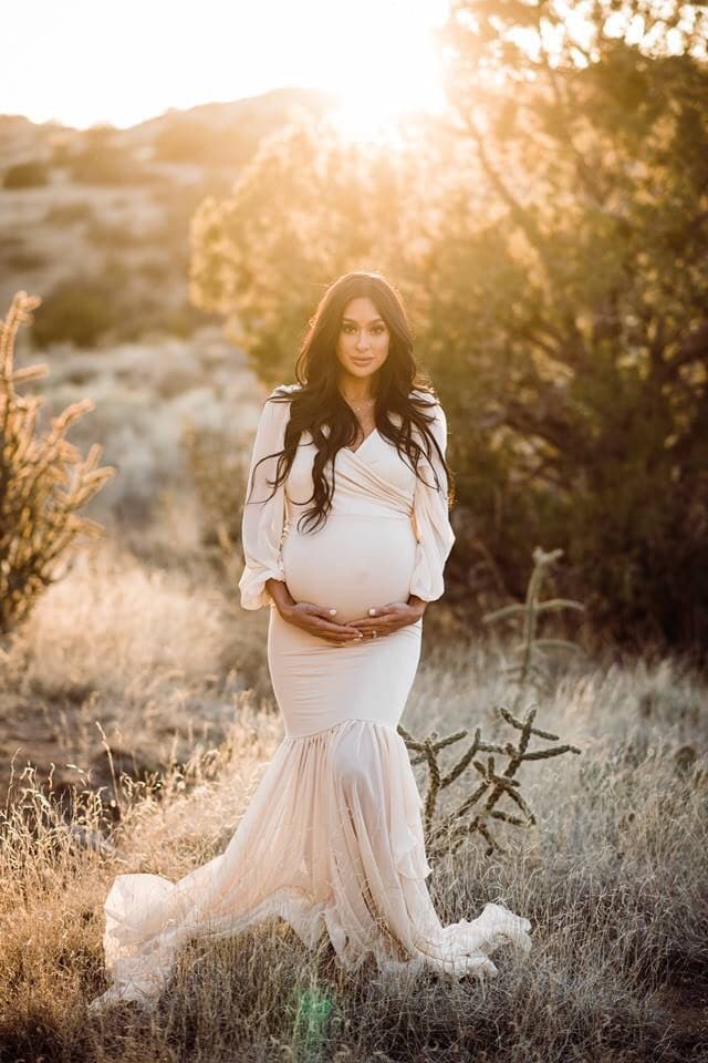 Pregnant mother wearing the Francis gown in champagne by Sew Trendy standing in a desert field at sunset