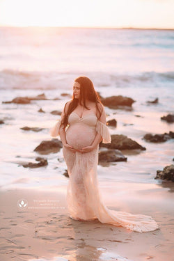 Pregnant woman in the Persephone Gown in Champagne by Sew Trendy Accessories standing on a beach.