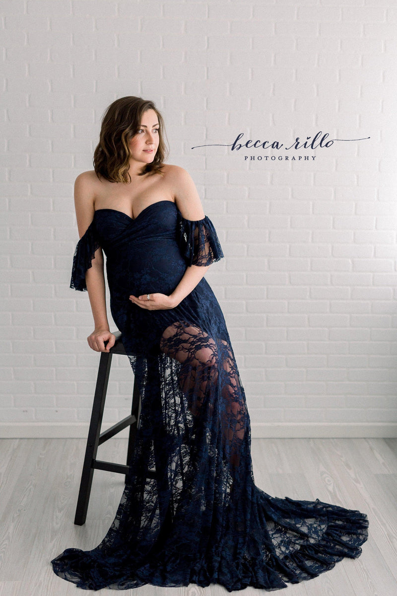 Pregnant woman in the Persephone Gown in Navy by Sew Trendy Accessories in the studio with a white brick background.