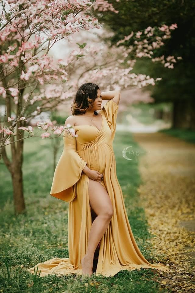 Expecting mother wearing Wren gown in gold by Sew Trendy standing in cherry blossoms