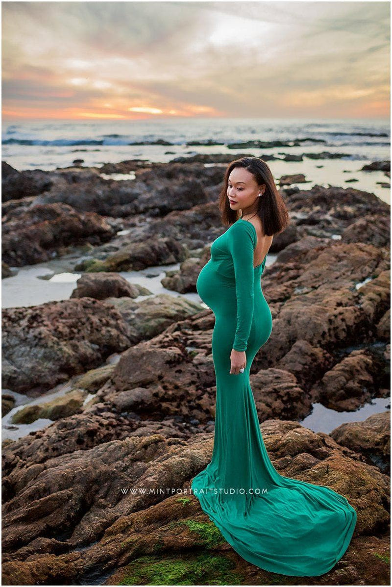 Pregnant mother in the Krysten Gown by Sew Trendy Accessories in Emerald on a beach with rocks.