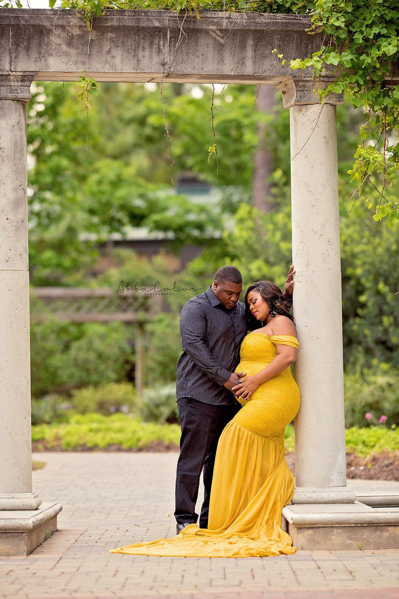 Expecting mother wearing the Amorah gown in gold by Sew Trendy with her husband standing in a garden.